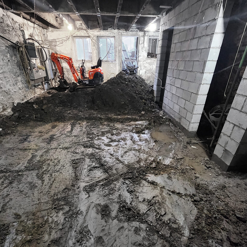Une mini-excavatrice et un convoyeur lors de travaux d'excavation en sous-oeuvre d'un bâtiment commercial.